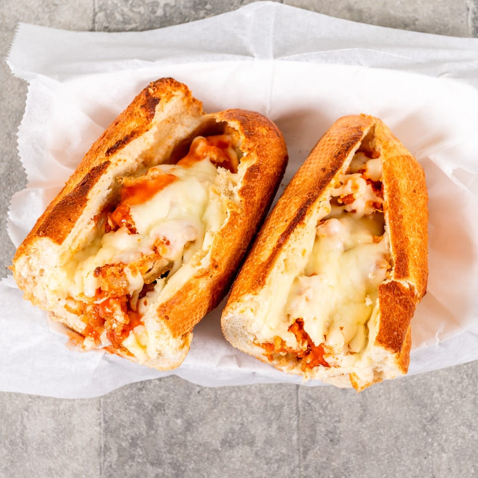Two halves of a cheesy chicken parmesan sub sandwich on white paper.