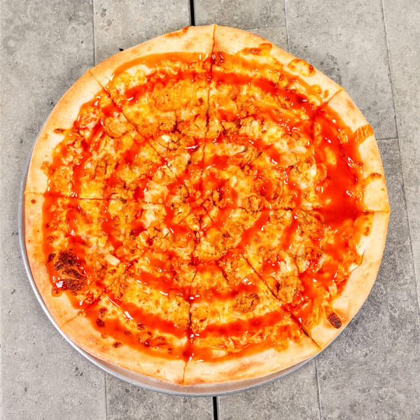 A whole buffalo chicken pizza, sliced into eight pieces, drizzled with hot sauce.