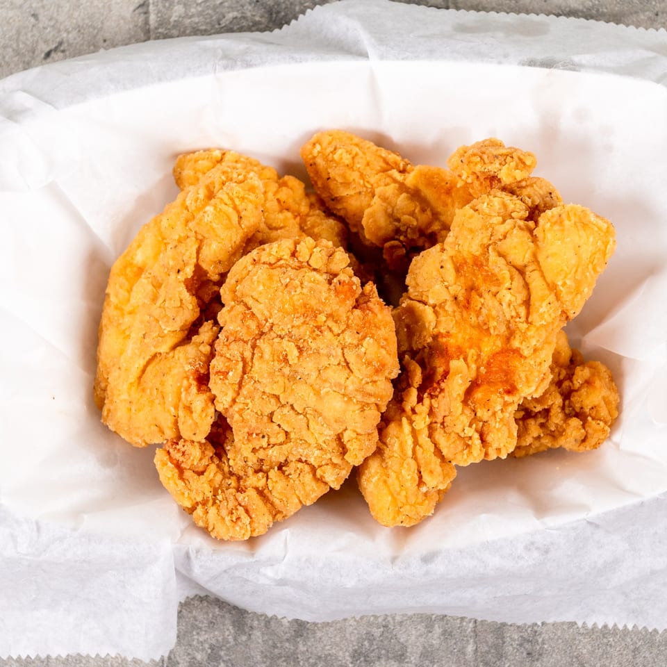 Golden-brown fried chicken tenders in a white paper-lined basket, viewed from above.