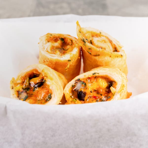 Four golden-brown, crispy fried spring rolls, cut in half, revealing a savory orange filling.