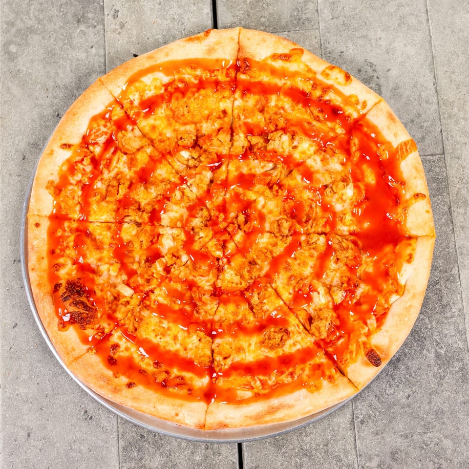 A whole buffalo chicken pizza, sliced, with a vibrant orange sauce drizzled over the top.