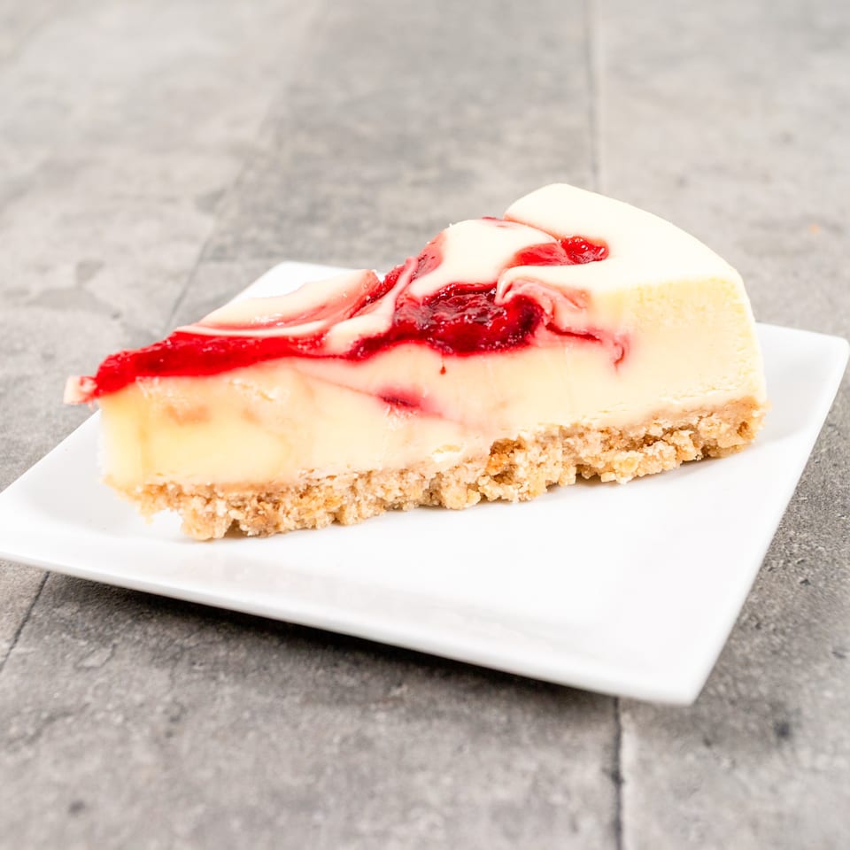 A slice of cheesecake with a graham cracker crust and swirled raspberry topping on a white plate.
