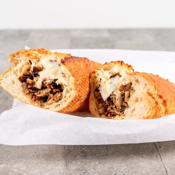 Two halves of a cheesy steak and mushroom sandwich on a white paper-lined tray.