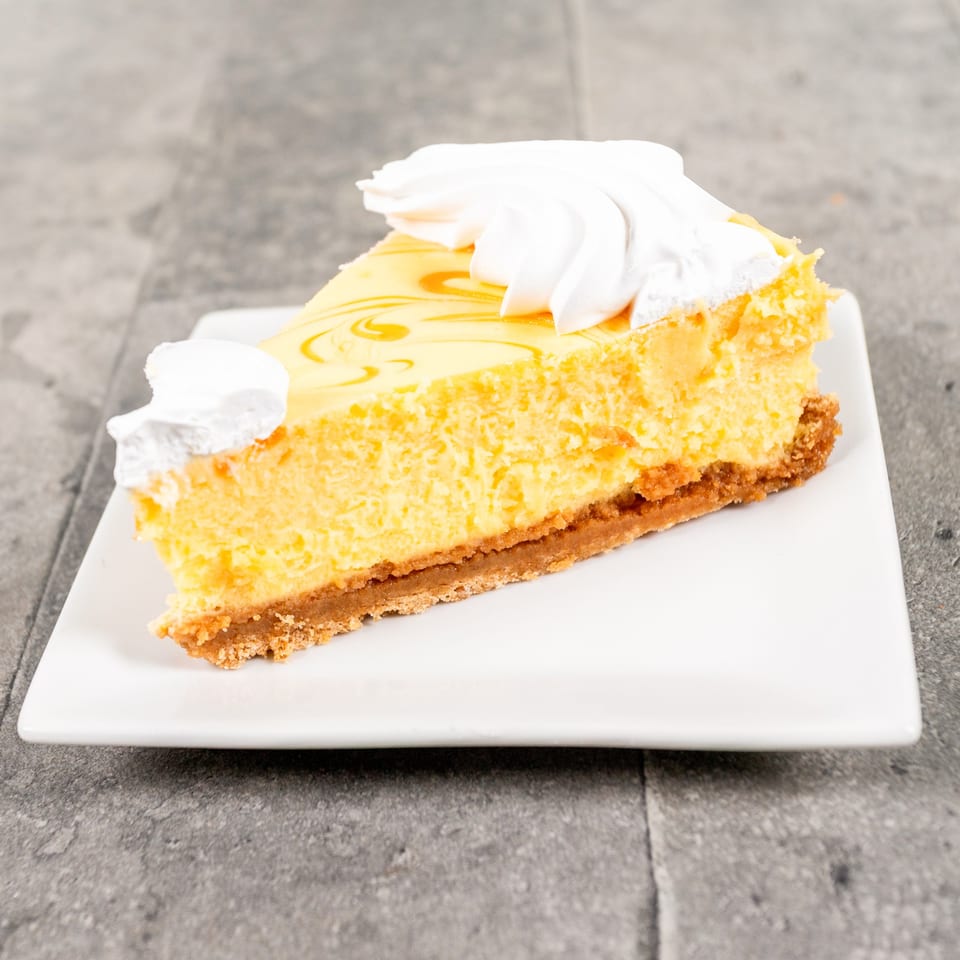 Slice of lemon cheesecake with a graham cracker crust, topped with whipped cream swirls.